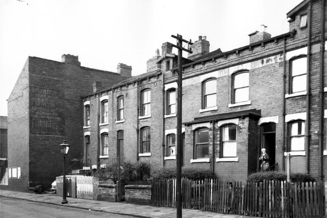Four back-to-back houses on Ascot Street with private gardens in front. On the left visible on the back wall of number 2 Ascot Place is a faded advert for furniture. A woman is in the doorway of 25. Pictured in October 1966.