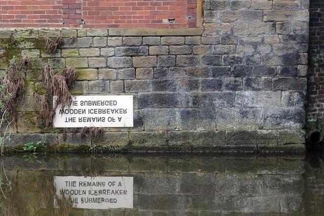 The sign on the Leeds and Liverpool Canal reads: 'The Remains of a Wooden Icebreaker Lie Submerged' and is found near the Leeds Industrial Museum, Armley Mills