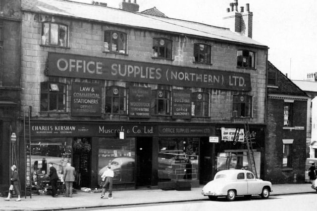 The south side of Park Lane pictured in June 1950. Premises in focus are C. Kershaw, nurseryman; Muscroft & Co. Ltd., wines and spirits; Office Supplies (Northern) Ltd.and P. Godlove, tailor. Pedestrians and a parked car are in front of the shops, which have two ladders propped against them.