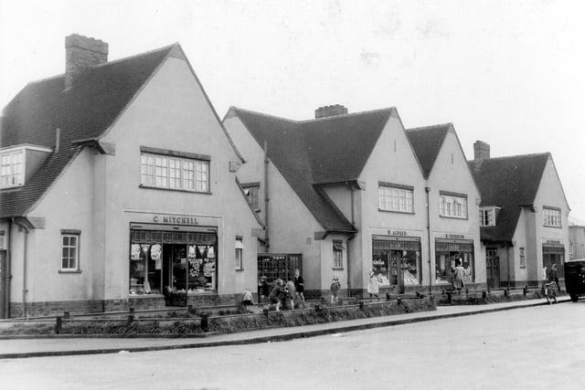 Parade of shops with living accommodation in August 1939. On the left is C. Mitchell, butcher at number 28. Number 26, Willie Aldred Greengrocer, next at number 24 Harry Thornton grocer. Last on the right, number 22 Alfred Thompson Fish & Chips. A number of children are playing on the grass verge. Pictured in August 1939.
