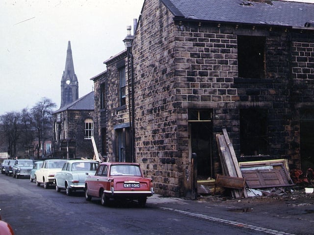 Houses on Brighton Square in the process of demolition, seen from Commercial Street, were also soon to be demolished; the area is now covered by Marshall Close. Cars are parked along Commercial Street and the spire of St. Mary's-in-the-Wood Church can be seen in the background. Pictured in May 1965.
