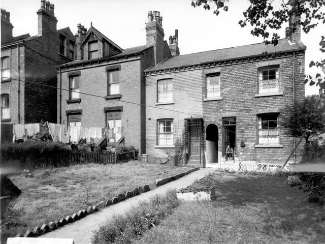A man sits on the doorstep at the back of South Mount Street. The houses have long back gardens and the gardens are separated by a communal path.  A clear view of the passageway through the arch can be seen.
