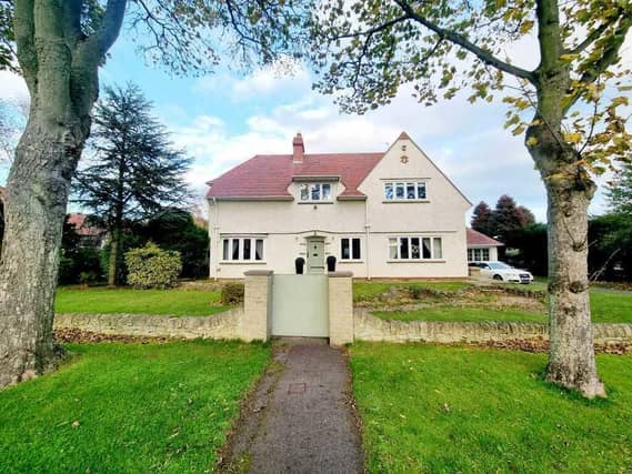 A front view of the detached home, within its lawned gardens.
