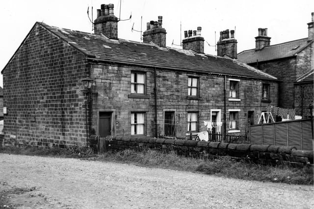 The rear private gardens and entrances of a row of terraced houses on Keighley Place. Clothes hang on lines stretched across the gardens. The road in the foreground is Keighley Place. Pictured in August 1963.
