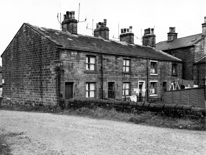 The rear private gardens and entrances of a row of terraced houses on Keighley Place. Clothes hang on lines stretched across the gardens. The road in the foreground is Keighley Place. Pictured in August 1963.