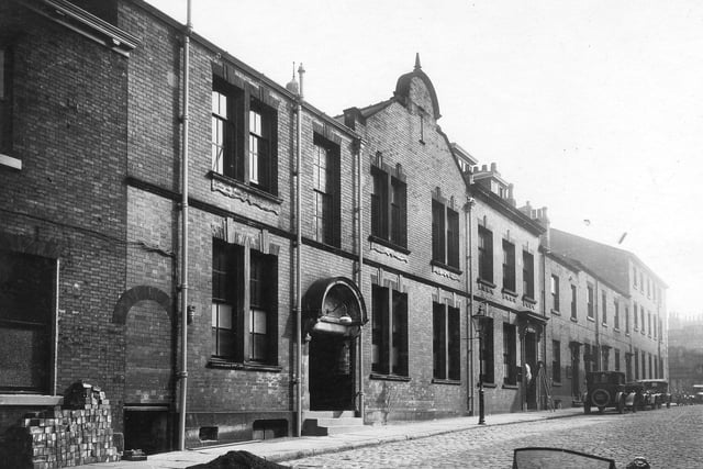 The Leeds Trades Hall on Upper Fountaine Street pictured in August 1927. The hall, run by J Clough, secretary, is divided into seven separate departments within the hall. Cars are parked further down the side of the cobble street..