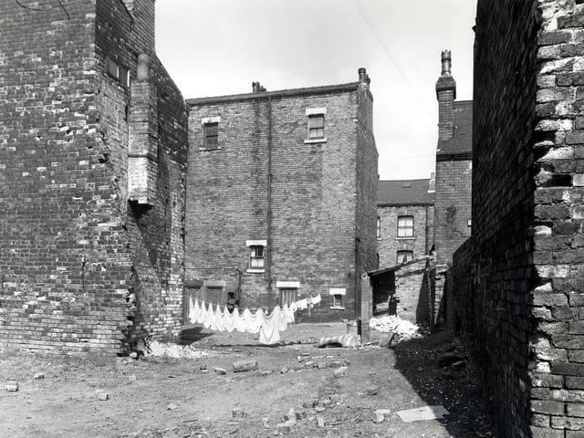 This view looks across an area of waste ground to the rear of numbers 68 and 70 Glover Street. To the left are the backs of numbers 8 and 10 Gerrans Street, which appear to be in the process of demolition, while on the right is an outside toilet. Pictured in July 1958.