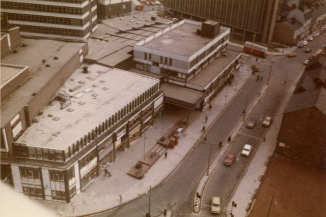 A bird's eye view looking down on the roof tops of the Merrion Centre with Merrion Street on the right. Rising above the Merrion Centre on the left is the office block Wade House, while the tall building towards the top right is Fairfax House on Wade Lane. An area of land has been cleared at the bottom right; the buildings next to it would also eventually be demolished to make way for the St. John's Centre, opened in 1985.