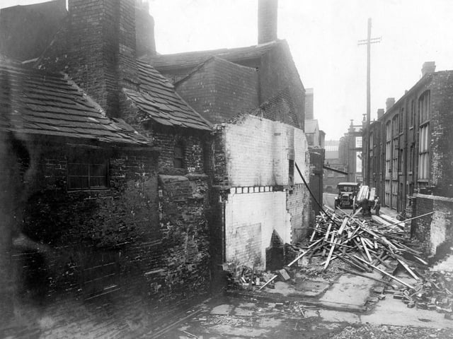 Unicorn Yard, off the Lower Headrow, looking north towards back Harrison Street. Some buildings have already been demolished and piles of bricks and wood are in the yard. Beyond two men are loading wood on to a cart with a car just behind them. Pictured in July 1928.
