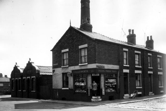 On the left of this image is the Times Sanitary Steam Laundry (Leeds) Ltd. At the corner at  is the Frank Wigglesworth English and Foreign Fruits Store, where a woman in an apron stands in the doorway. On the right are two back to back houses on Temple View Place where a pram is parked outside one of them.  Pictured in July 1963.