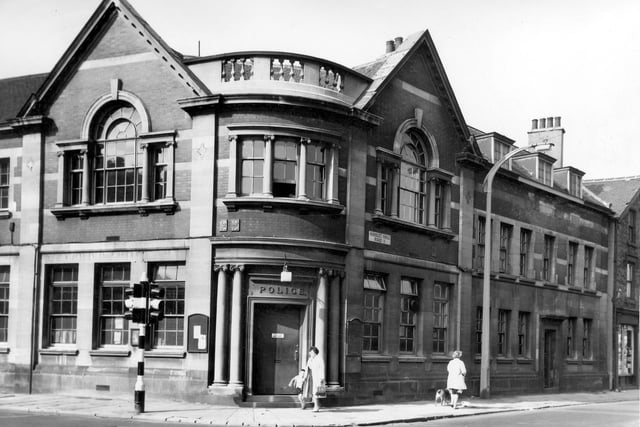 The Police Station at the junction of Hunslet Hall Road and Dewsbury Road. A woman walks past the door with a young boy in short trousers while on the right a woman walks down Hunslet Hall Road with a dog. On the left is a set of traffic lights painted in black and white stripes. Pictured in August 1964.