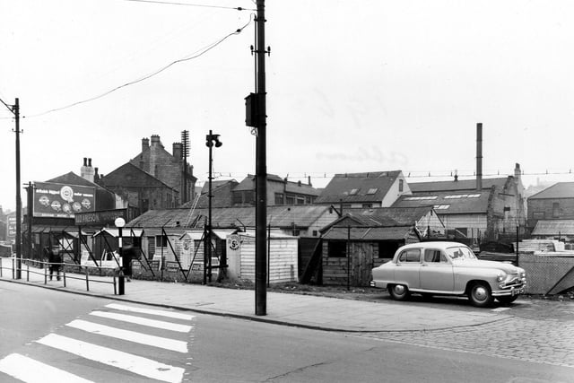 A view of L.& D. Ableson, timber merchants, on Sheepscar Street North in July 1954. The yard has lots of garden sheds for sale. In the foreground is a zebra crossing and a belisha beacon. A car is parked on the right. An advertisement for a motor concern is visible on the left.