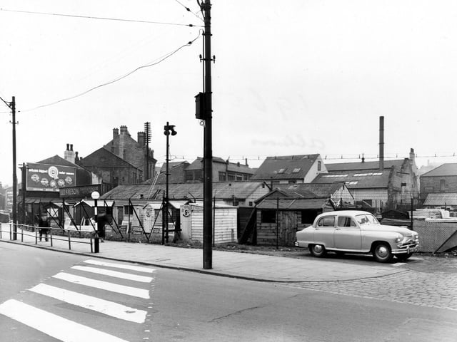 A view of L.& D. Ableson, timber merchants, on Sheepscar Street North in July 1954. The yard has lots of garden sheds for sale. In the foreground is a zebra crossing and a belisha beacon. A car is parked on the right. An advertisement for a motor concern is visible on the left.