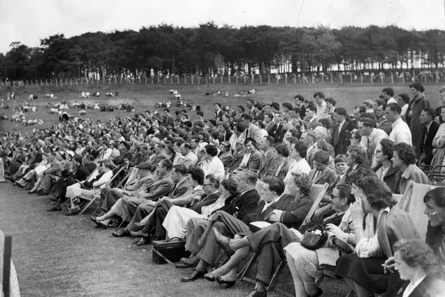 A section of the crowd at the exhibition tennis match at Temple Newsam in June 1955. The spectators nearest the front are seated on deckchairs while those behind are either standing or lounging on the grass in the background.