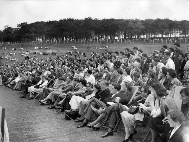 A section of the crowd at the exhibition tennis match at Temple Newsam in June 1955. The spectators nearest the front are seated on deckchairs while those behind are either standing or lounging on the grass in the background.