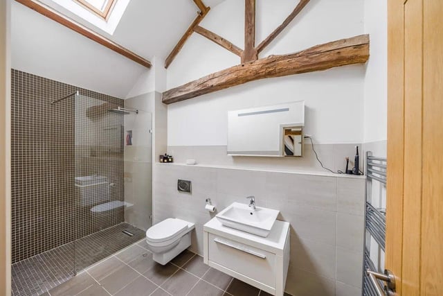 The stunning house bathroom has a three-piece white suite with a separate shower cubicle, stylish tiled walls and flooring, exposed wooden beam and a skylight window.