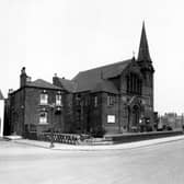 Hunslet Carr Methodist church on Moor Road with two sections of the wall collapsed. A streetlamp is in the foreground and an advertisement for Capstan tobacco can be seen on the gable end of a building in the background. People are walking along the street. Pictured in April 1948.