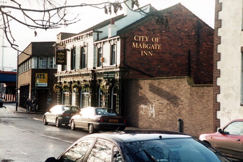 A view down Mabgate in March 2002 towards the inner city ring road with the City Of Mabgate Inn on the right. The Inn with its green tile facade dates back top circa 1857 and has a cholera burial ground opposite. The building behind is the ATS Euromaster and two people are walking past.