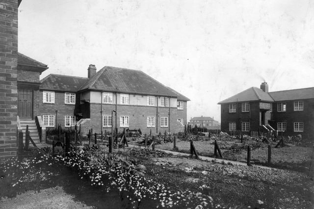 Maisonettes on Throstle Road, on the Middleton housing estate. A number 43 is beside the door on the left-hand side. The central block houses numbers 45, 47, 49 and 51. There is still some building rubble among the newly-established vegetable plots, but flowers are in bloom in the foreground. Two women can be seen talking outside the flats towards the right, (numbers 49 and 51). On the right, part of the block housing numbers 53 to 63 is visible. Pictured in September 1932.
