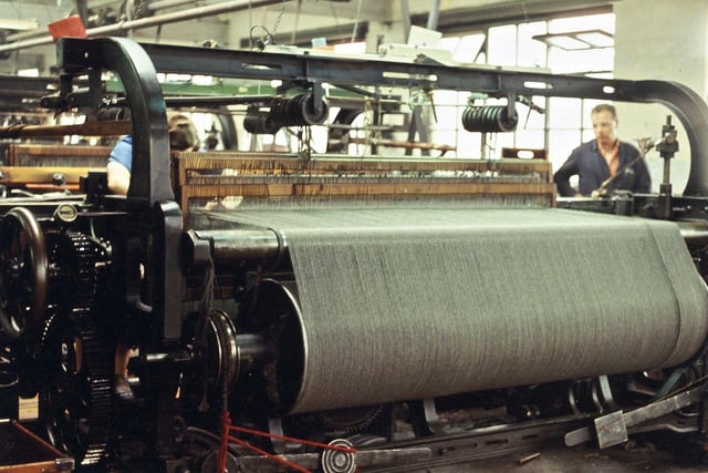 An old-fashioned plain loom at Prospect Mills, showing a loom tuner at work on the right hand side. Plain looms were often used to weave cloth that required a woollen warp, (as seen here), as their action was not as rapid as the automatic looms and they could be stopped more easily should the warp threads break and need tieing again.