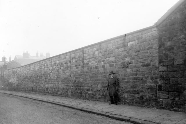 A man stands in front of a high wall on Alma Road in February 1936. In the distance can be seen a cupola with weathervane on top.