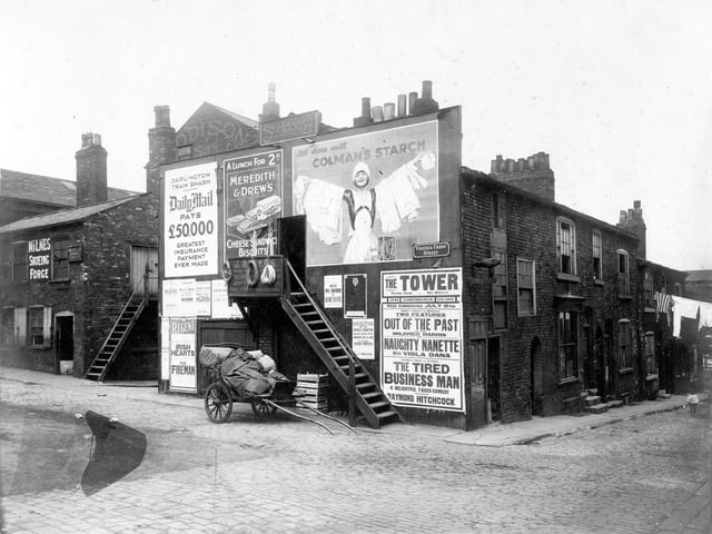 Virginia Cross Street was at the junction of Harewood Street and Nelson Street, which is on the right. To the left, forge belonging to William Milnes, shoeing smith, with outside stairs to upper floor. In the centre, wooden stairs lead to doorway, premises of J.Rogers a saddlery goods dealer. He has coils of rope hung over his business sign. A loaded hand cart can be seen. Pictured in July 1928.