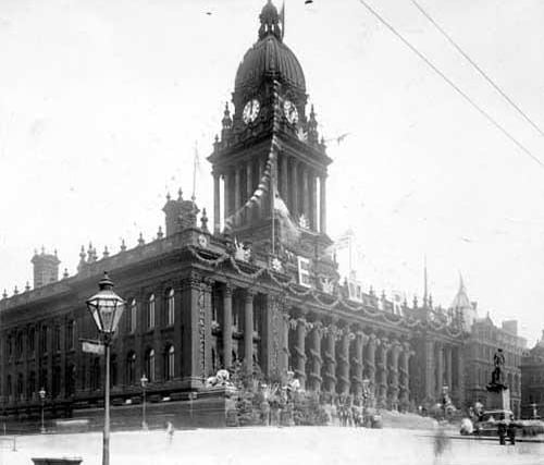 Leeds Town Hall decorated in August 1902 for the Coronation of Edward VII. The facade has hanging baskets, swagging and plants. To the left, a statue of Sir Robert Peel, now located on Woodhouse Moor. This view is from Oxford Place and looks at the south side.