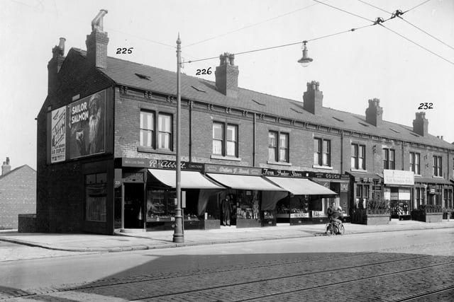 To the left is the junction with Glenthorpe Terrace. Then confectionery shop, owner R. Abbott at no.221. Next no.223, George Arthur Reed, draper. Farm Produce Store is no.225. At the end of the row, no.227 ladies Hairdresser. On the gable end of the building, a poster for Sir Alan Cobham's air circus, one for 'sailor' brand salmon. Pictured in September 1935.