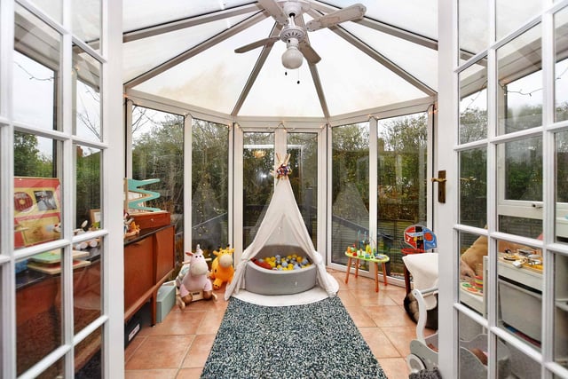 A cosy living room with double doors leading to conservatory, currently being used as a playroom with doors to rear garden.