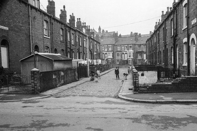 A view looking along Back Gipton Avenue from Gathorne Terrace in 1969. Backs of houses on Gipton Terrace are on the left while on the right are houses which face on to Gipton Avenue. Several children of varying ages are seen playing in the street. Houses running along in the background are on Bankside Street.
