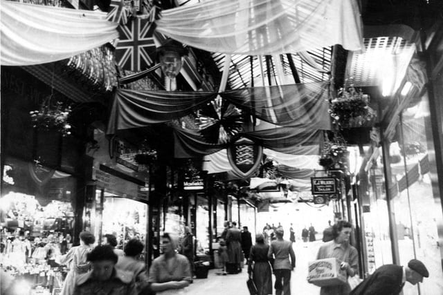 Coronation decorations in the Queens Arcade. The arcade was built in 1889 on the site of the Old Rose and Crown public house. It was designed by Edward Clark of London. A second tier of shops could be entered from the wrought iron balconies.