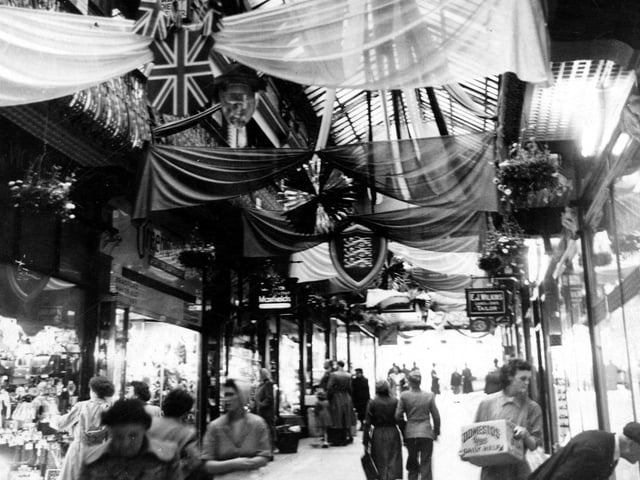Coronation decorations in the Queens Arcade. The arcade was built in 1889 on the site of the Old Rose and Crown public house. It was designed by Edward Clark of London. A second tier of shops could be entered from the wrought iron balconies.