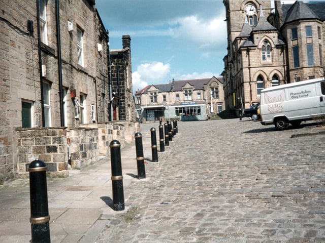 Yeadon's Devonshire Place, used as a car park. Shops on the left front onto the High Street. This is looking across the Town Hall Square, with Yeadon Town Hall to the right. The building in the centre is Yeadon library in what was formerly a branch of Leeds Industrial Co-operative Society - Co-op grocers.