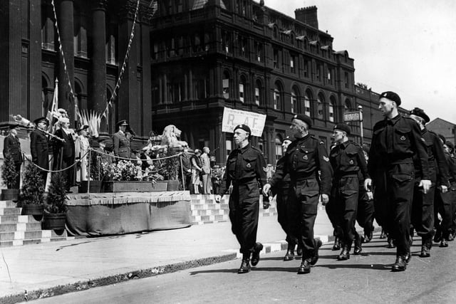March past, part of Leeds Wings For Victory campaign in June 1943. A contingent of Civil Defence workers are marching along The Headrow. Air Commodore G.A. Walker D.S.O., D.F.C. is taking the salute. A banner in front of the Central Library advertises an exhibition of Royal Air Force War photographs.