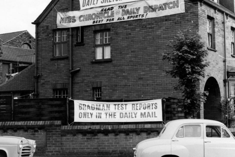 July 1956 and pictured is the gable end of house on St.Michael's Lane. Advertisements for various newspapers with particular reference to test match reports are hanging from the wall of the house and the fence in front.