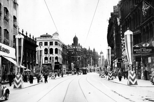 Coronation decorations on Boar Lane, looking towards Vicar Lane. On the left is a corner of C. and A. clothes store, then Holy Trinity Church. The sign for Schweppes drinks is displayed at 148 Briggate, the junction with Boar Lane. On the right, the canopy for Walter Fairburn's White Horse Restaurant can be seen.