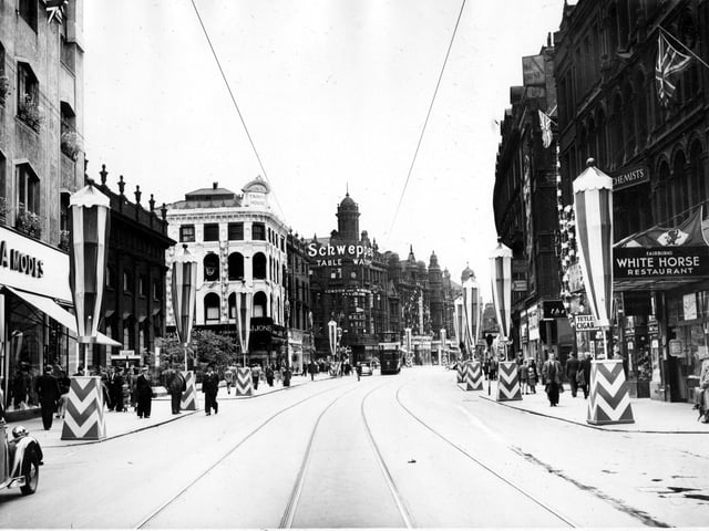 Coronation decorations on Boar Lane, looking towards Vicar Lane. On the left is a corner of C. and A. clothes store, then Holy Trinity Church. The sign for Schweppes drinks is displayed at 148 Briggate, the junction with Boar Lane. On the right, the canopy for Walter Fairburn's White Horse Restaurant can be seen.
