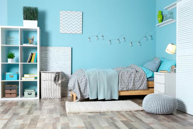 A modern child's room with coloured walls, bookshelves and storage, laundry basket and rug.