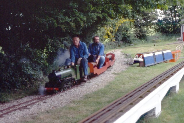 Two men are seen riding on the miniature steam locomotive.  They are pictured in June 1995.