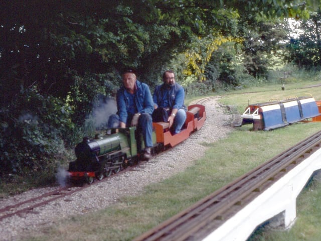 Two men are seen riding on the miniature steam locomotive.  They are pictured in June 1995.