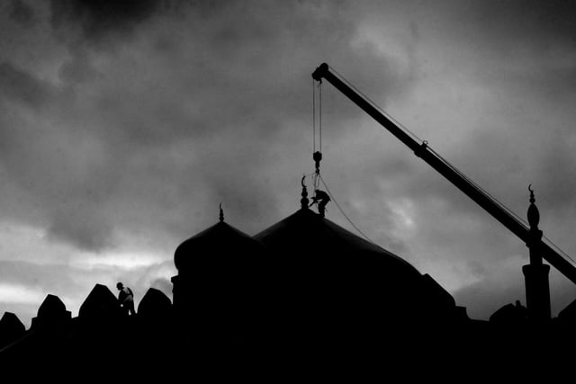 A workman carefully works on top of the Jamia Masjid Bilal temple on Harehills Lane. He's tied on with safety lines from a nearby crane as he works to reinstall a new moon on top of the dome which fell off during some recent strong winds.