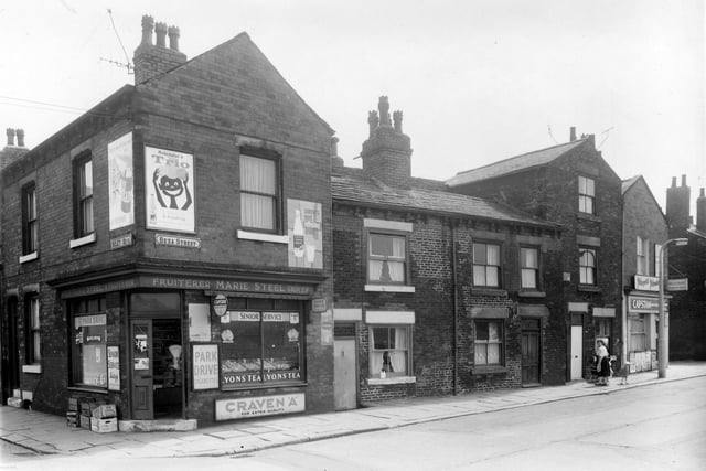 On the left is the corner with Riley Street and shop also on Beza Street. Selling groceries, fruit and cigarettes, run by Marie Steel. Moving right, unseen in this view, a passage way leads to Thackeray Court which lay behind Beza Street. Then a newsagents shop is at the junction with Tulip Terrace on the right.