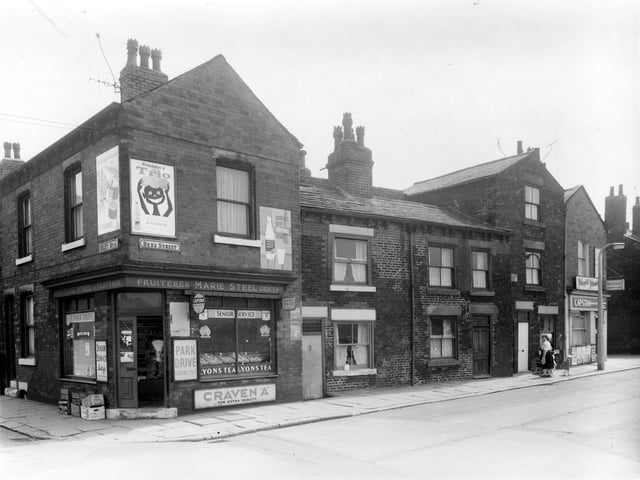 On the left is the corner with Riley Street and shop also on Beza Street. Selling groceries, fruit and cigarettes, run by Marie Steel. Moving right, unseen in this view, a passage way leads to Thackeray Court which lay behind Beza Street. Then a newsagents shop is at the junction with Tulip Terrace on the right.