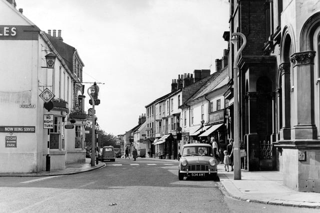 High Street at the junctions with Horsefair, left, and Bank Street, right, in September 1962. The Angel Hotel, an old posting inn is at number 30 High Street, on the left. Two other public houses are visible on the right, the Red Lion at number 19 and the Crown Hotel at number 25 at the junction with Cross Street. The National Westminster Bank in the foreground, far right, is number 49 High Street, on the corner with Bank Street.