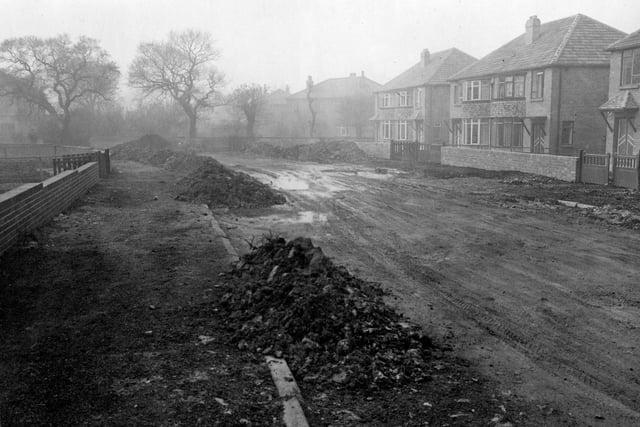 An unmade road on Carr Manor Avenue in October 1953. Semi-detached houses can be seen to the right of the picture. Newly built red brick walls have been built around the front of the gardens to the left and right.