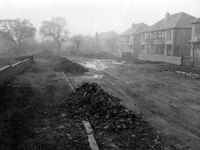An unmade road on Carr Manor Avenue in October 1953. Semi-detached houses can be seen to the right of the picture. Newly built red brick walls have been built around the front of the gardens to the left and right.