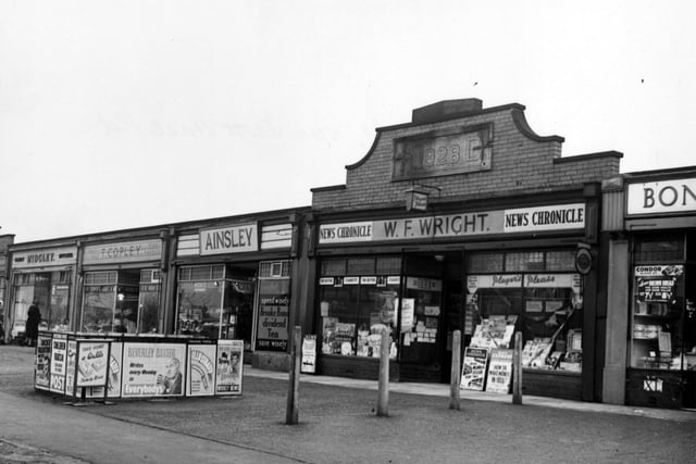 Shops on Scott Hall Road, 540 W F Wright, newsagent, with advertisements for various newspapers outside. A brick wall above the shop has a plaque with inscription, 1928 A D 542 Ainsley, Edwin, baker, with advertisements for Brooke Bond tea and Hovis. Two women are outside the entrance to shop. Pictured in February 1955.