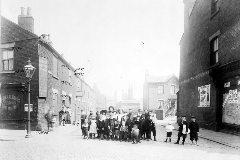 Taken from Waterloo Road, looking down Bower Row prior to the Waterloo Road improvements in August 1904. On the right is an empty unidentified retail premises, next to this is a large poster advertising Taylor's Drug Co. Further down the street is a house called Claremont House which has wooden carts in the yard. Towards the rear of the street, which is a cul-de-sac, it is possible to see the rear of the Grey Mare Inn which is located on Low Road beyond. On the opposite (left) side of the road there is a sign for W. Cutts, Drainer and Builder, who lived at number 2 Bower Row. On the corner with Waterloo Road is an advertisement for the Hunslet Knitting Shop outside of H. Houlding Ltd. Hosier