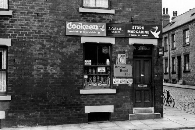 Wolseley Road in August 1955. The shop at No.11 was owned by A. Carnall, grocer. Above the door are signs for Stork Margarine and Cookeen in the window. There are jars of loose sweets visible. To the side of the shop is a bicycle on the stone set road.
