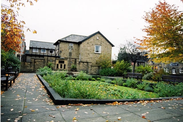 Looking from the direction of Bondgate at the Garden of Remembrance in October 2003. The garden is surrounded by a paved area with wooden seating. The Memorial Cross, situated at the rear of the planted area, was moved here from the Parish Churchyard after the the second world war. A series of four commemorative plaques are set into the rear wall. On the far left, the Curlew Cafe at numbers 11 to 13 Crossgate is visible.
